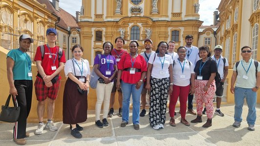 A group of scholars standing in front of Melk Abbey, the yellow monastery in the background
