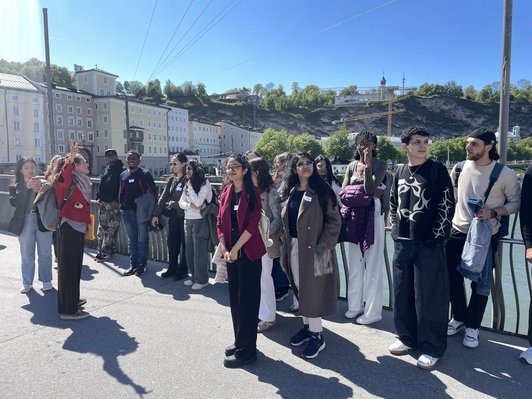 A group of scholarship holders standing outside in the city of Salzburg, listening to a tour guide