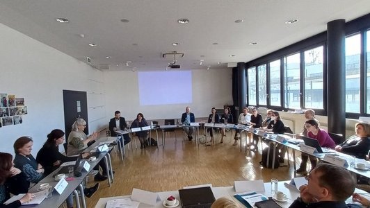 Mehrere Menschen sitzen im Kreis am Tisch und diskutieren.