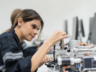 junge Frau in Arbeitskleidung bedient technisches Pult mit Verkabelung