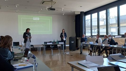 Zwei Frauen halten eine Präsentation und projizieren die erste Folie auf den Wand.