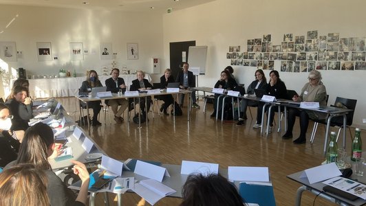 Menschen sitzen am Tisch in einem Form von geschlossenem U und diskutieren.