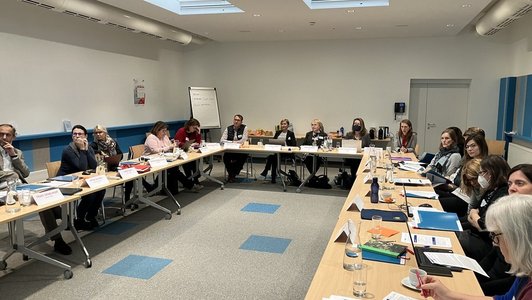 Große Gruppenphoto von am Tisch im Saal sitzenden Teilnehmerinnen des Österreichischen EQAVET Peer Reviews in Wien.