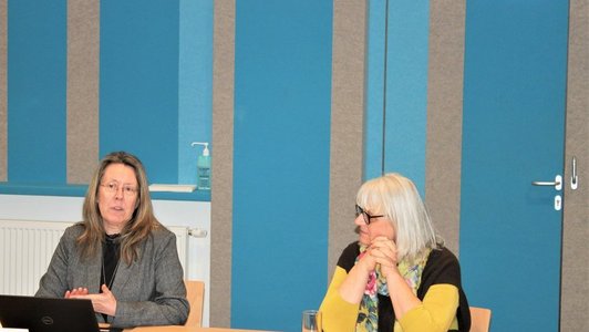 Zwei Frauen sitzen am Tisch im Saal und präsentieren die Ergebnisse.